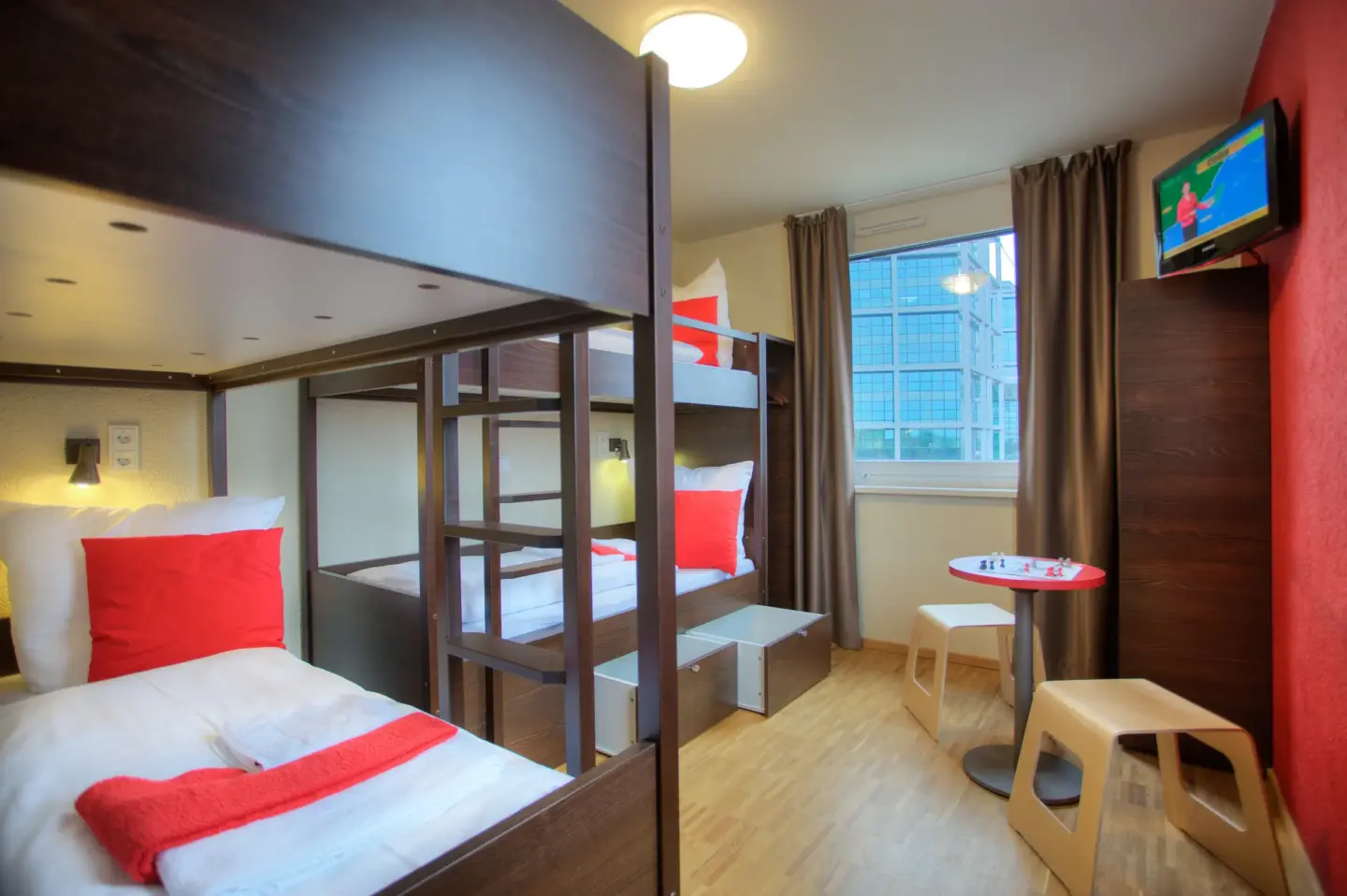 Klassenfahrt Berlin - Mehrbettzimmer mit zwei dunklen Doppelstockbetten, TV und Tisch