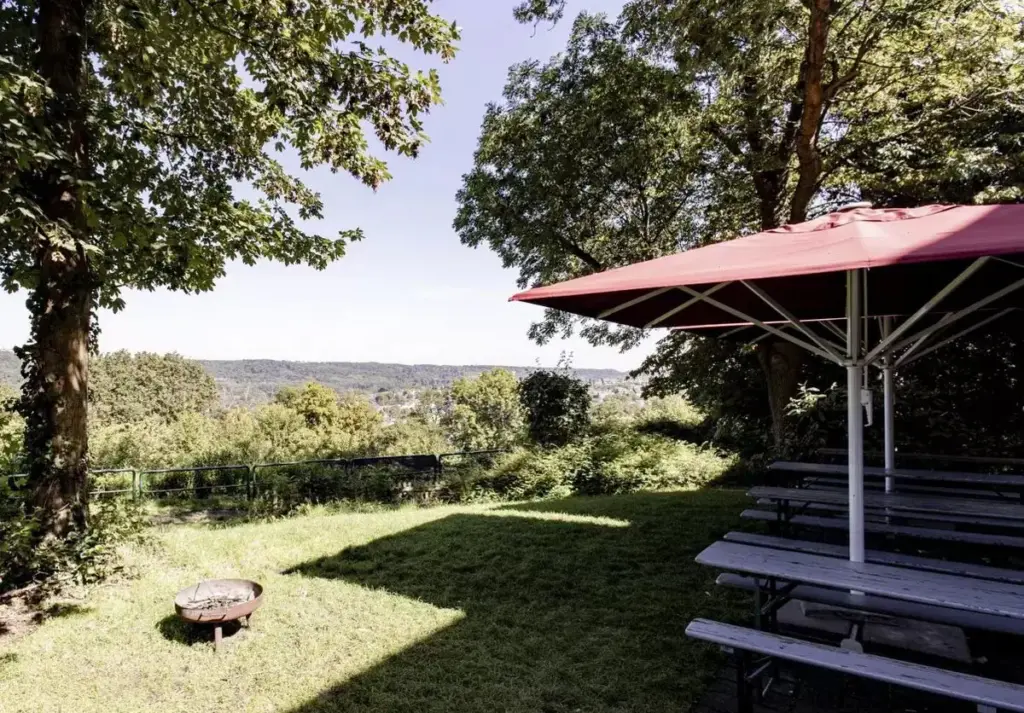 Klassenfahrt Essen - grüner Außenbereich der Jugendherberge mit Sonnenschirmen und Bänken