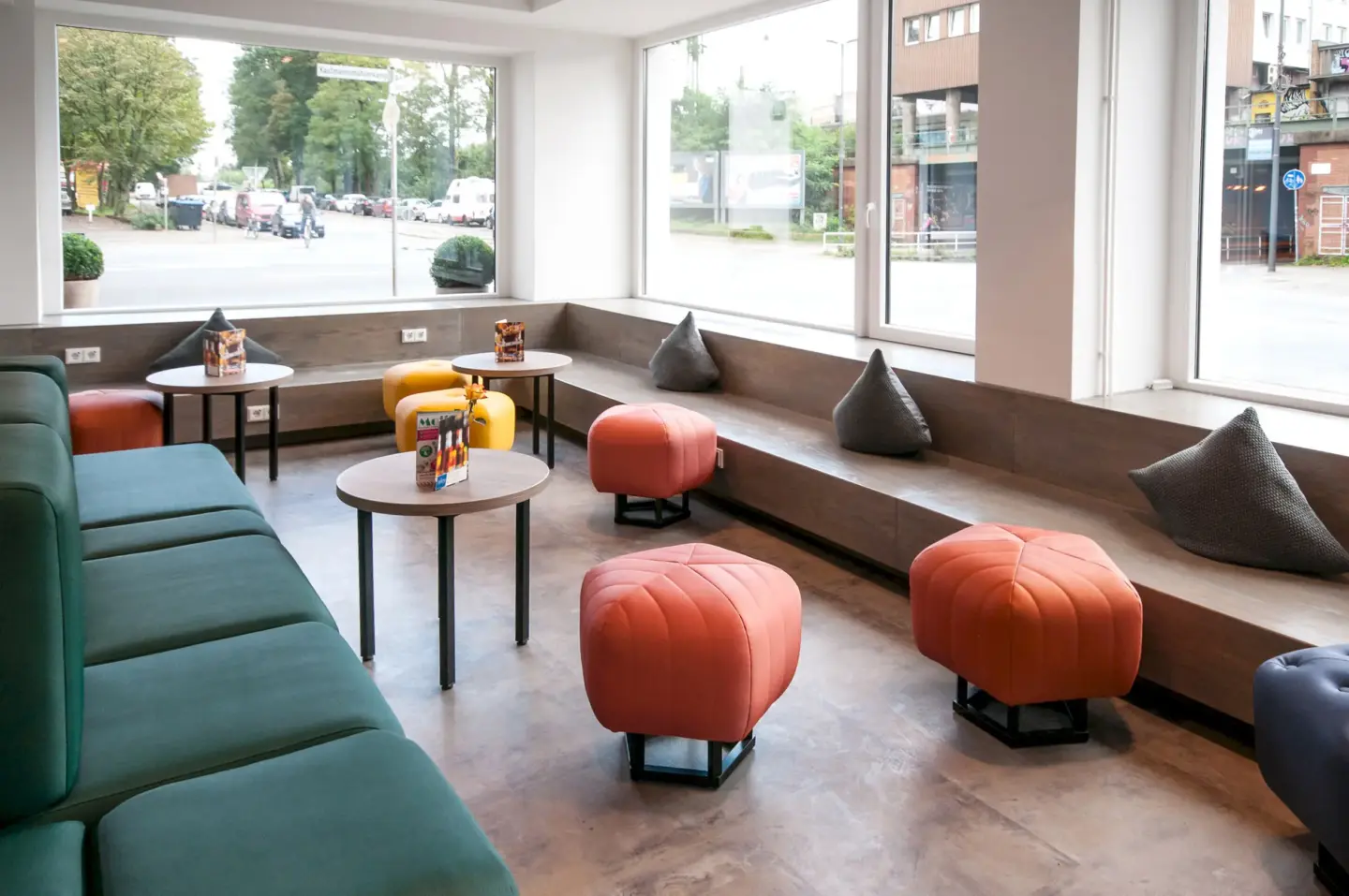 Klassenfahrt Bremen - in der Lounge steht lange Holzbank am Fenster, davor bunte Hocker und ein Sofa