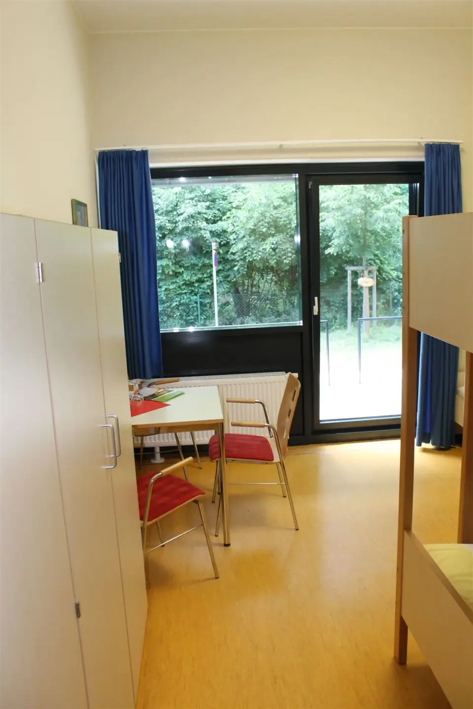 Klassenfahrt Dessau - Mehrbettzimmer mit Schrank, Tisch, Stühlen und Doppelstockbett